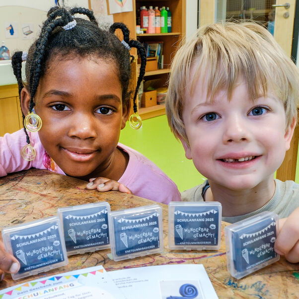 Zwei Kinder schauen in die Kamera und halten Päckchen mit Radierknete in den Händen.