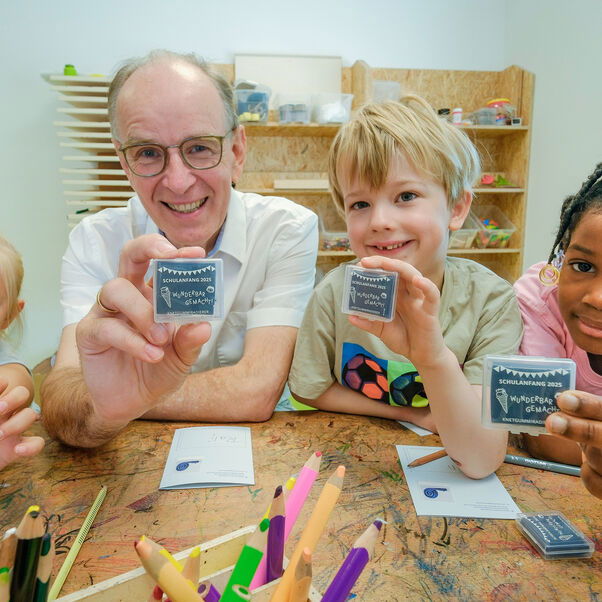Drei Kinder und eine männlich zu lesende Person halten Radiergummis in die Kamera.