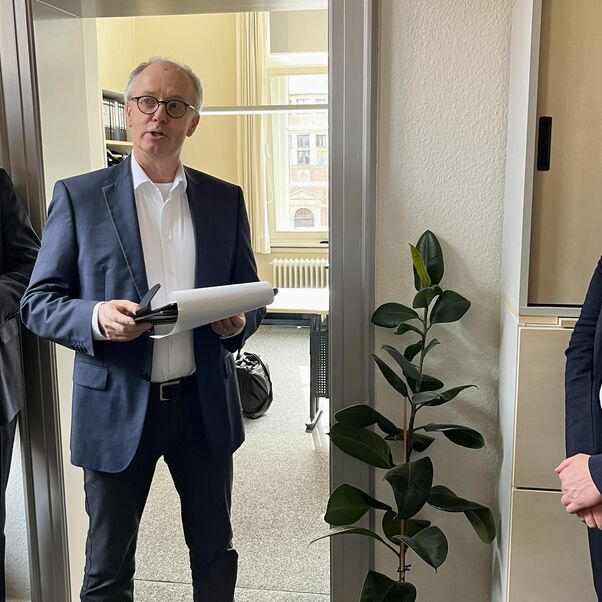 Drei Personen stehen in einem Büro und sprechen miteinander. 