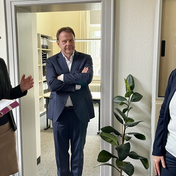 Drei Personen stehen in einem Büro einander gegenüber und sprechen miteinander.