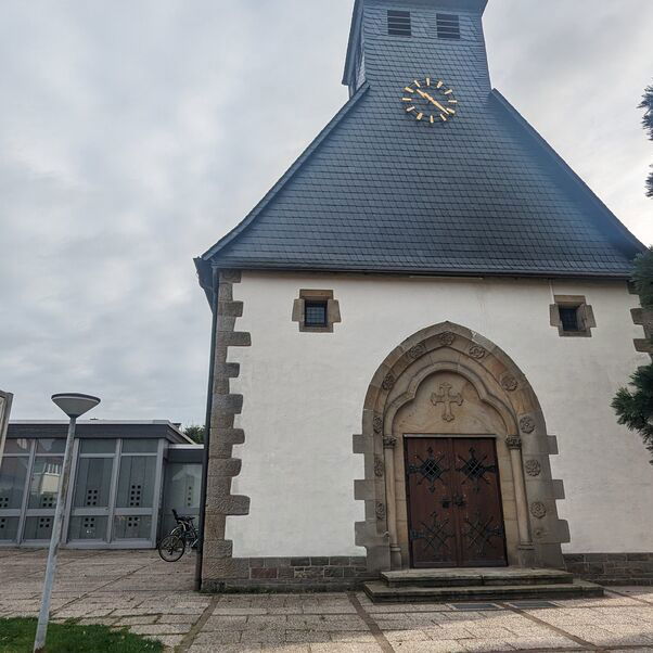 Blick auf einen Schaukasten auf dem Kirchplatz vor einem Kirchengebäude.