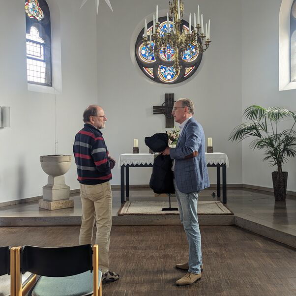 Zwei Männer stehen im Altarraum einer Kirche und unterhalten sich.