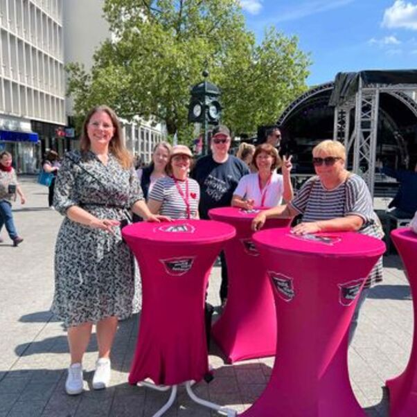 Vier Personen stehen in der Fußgängerzone hinter Stehtischen.
