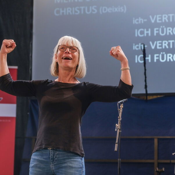 Eine weiblich zu lesende Person steht auf einer Bühne und gebärdet ein Lied.