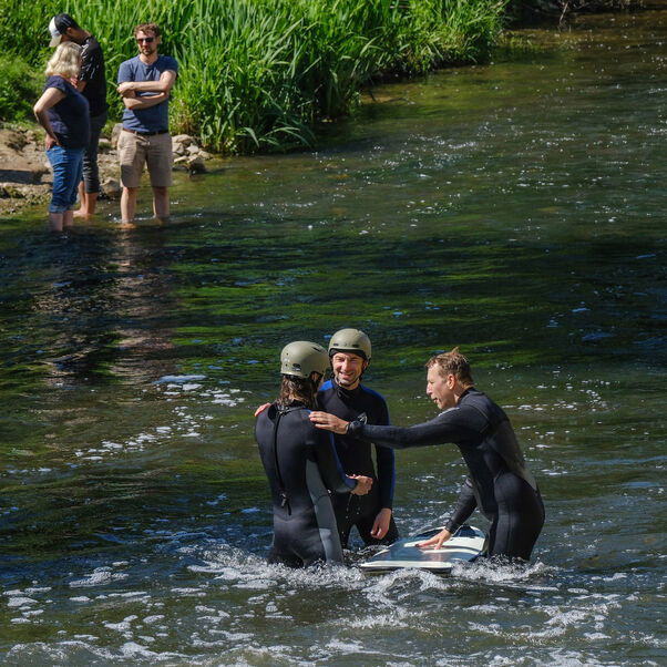 Drei Personen stehen in Neoprenanzügen im Wasser.