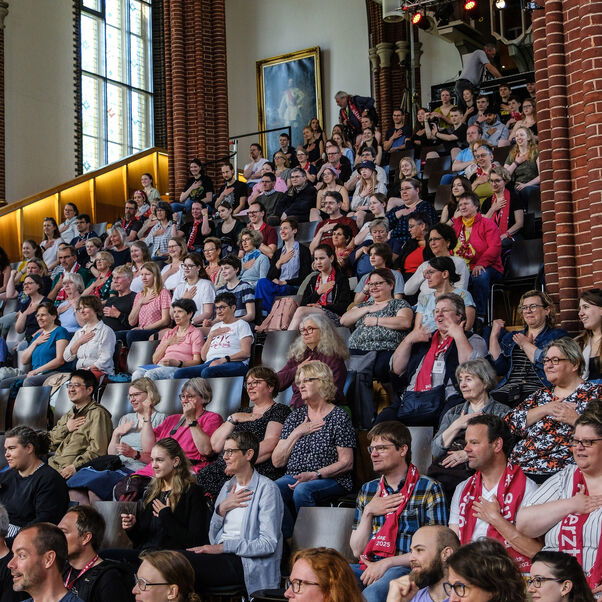 Menschen sitzen in einer Kirche auf einer Tribüne und singen mit Gebärden.