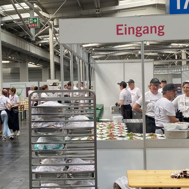 In der Küche des gläsernen Restaurants, die von außen einsehbar ist, bereiten Personen Essen zu.