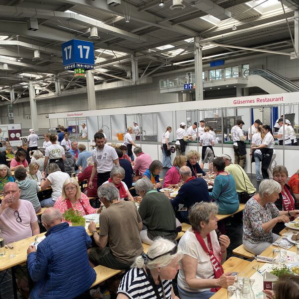 An langen Tischen sitzen viele Personen und essen.