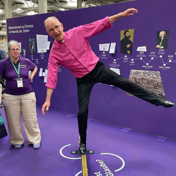 Eine männlich zu lesende Person balanciert auf einem Bein auf einem schmalen Balken.