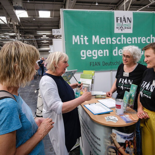 Weiblich zu lesende Personen unterhalten sich an einem Messestand.