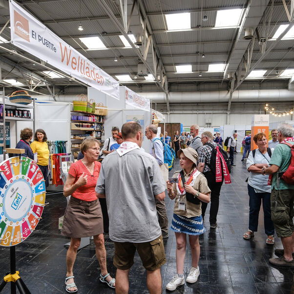 Personen gehen zwischen Messeständen hindurch.