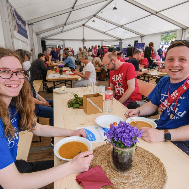 Eine weiblich und eine männlich zu lesende Person sitzen an einer Bierzeltgarnitur in einem Zelt.