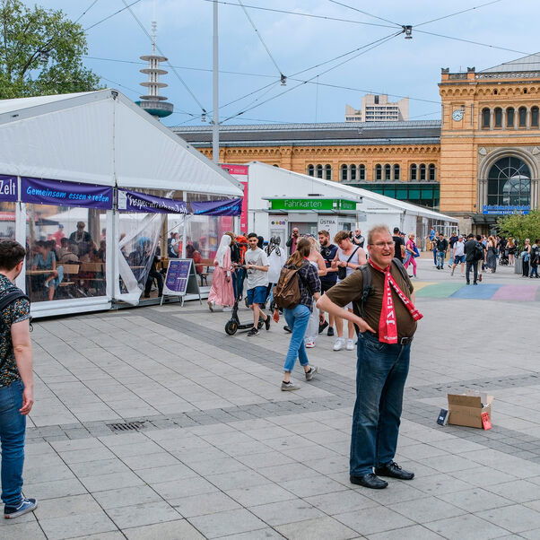 Vor dem Hauptbahnhof in Hannover steht ein Zelt, in dem Menschen an Bierzeltgarnituren sitzen.
