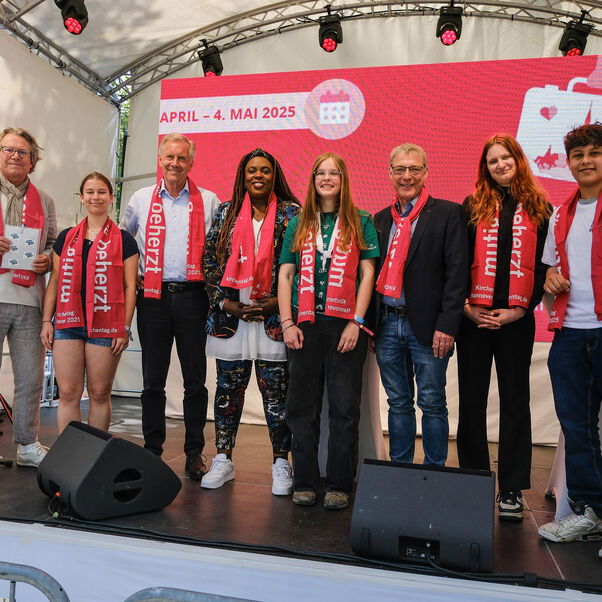 Eine Gruppe von weiblich und männlich zu lesenden Personen stehen in einer Reihe auf einer Bühne.