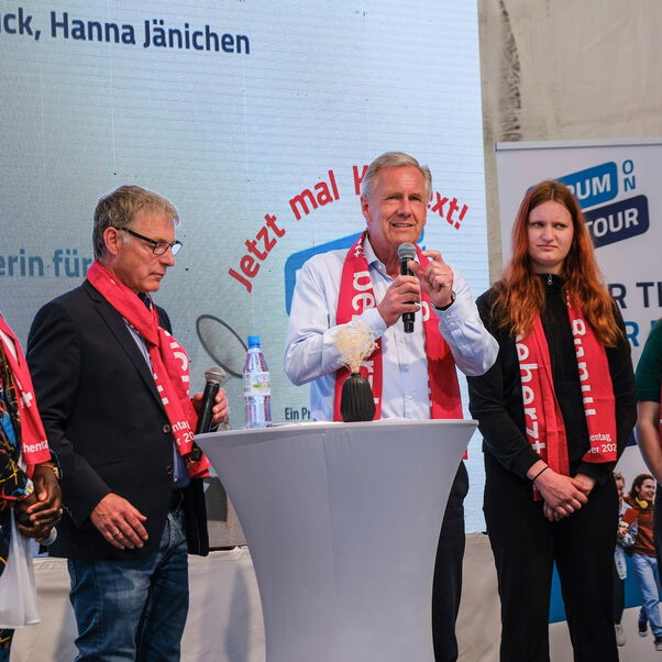 Zwei männlich zu lesende Personen und drei weiblich zu lesende Personen stehen an Stehtischen in einer Interviewsituation.