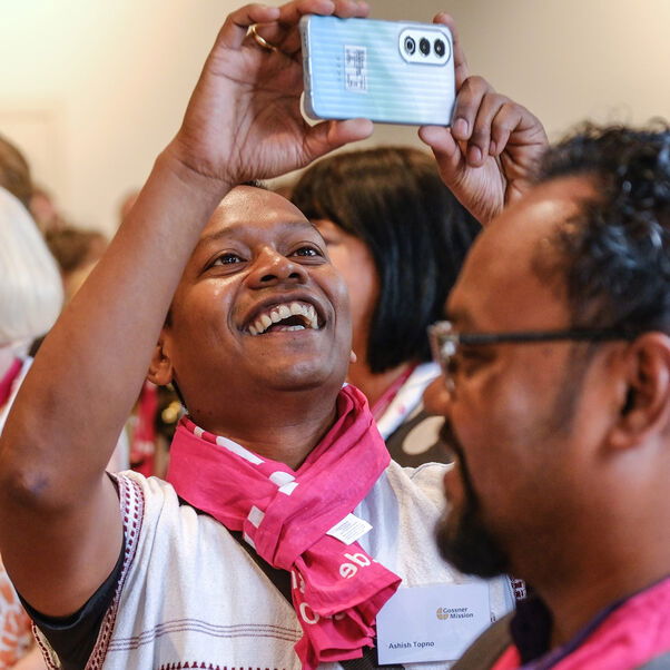Ein weiblich zu lesende Person steht mitten in einer Menschenmenge und macht ein Selfie.