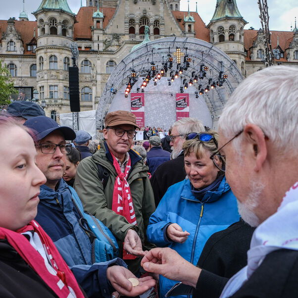 Eine männlich zu lesende Person teilt Abendmahlshostien aus bei einem Openair-Gottesdienst.