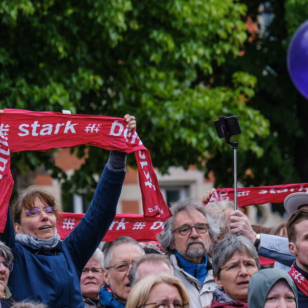 Eine große Gruppe von Menschen hält rote Schals in die Höhe.