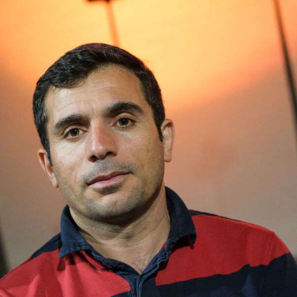 Eine männlich gelesene Person mit dunklen Haaren in rot-schwarzem Pulli.