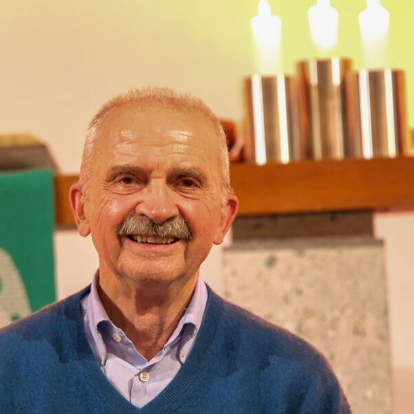 Eine männlich gelesene Person mit Schnurrbart in blauem Shirt mit karierten Hemden.