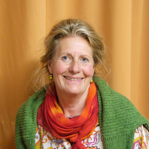 Eine weiblich gelesene Person mit blonden Haaren und rot-orangenem Schal mit grüner Strickjacke.