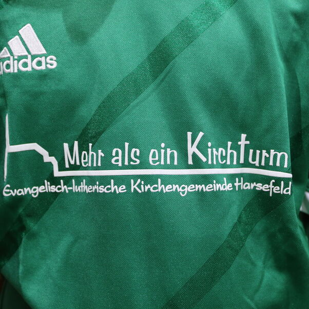 Ein grünes Trikot in Nahaufnahme, darauf steht: Mehr als ein Kirchturm - ev.-luth. Kirchengemeinde Harsefeld.