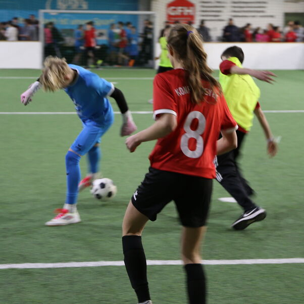 Szene beim Indoor-Fußball: drei Personen kämpfen um den Ball.