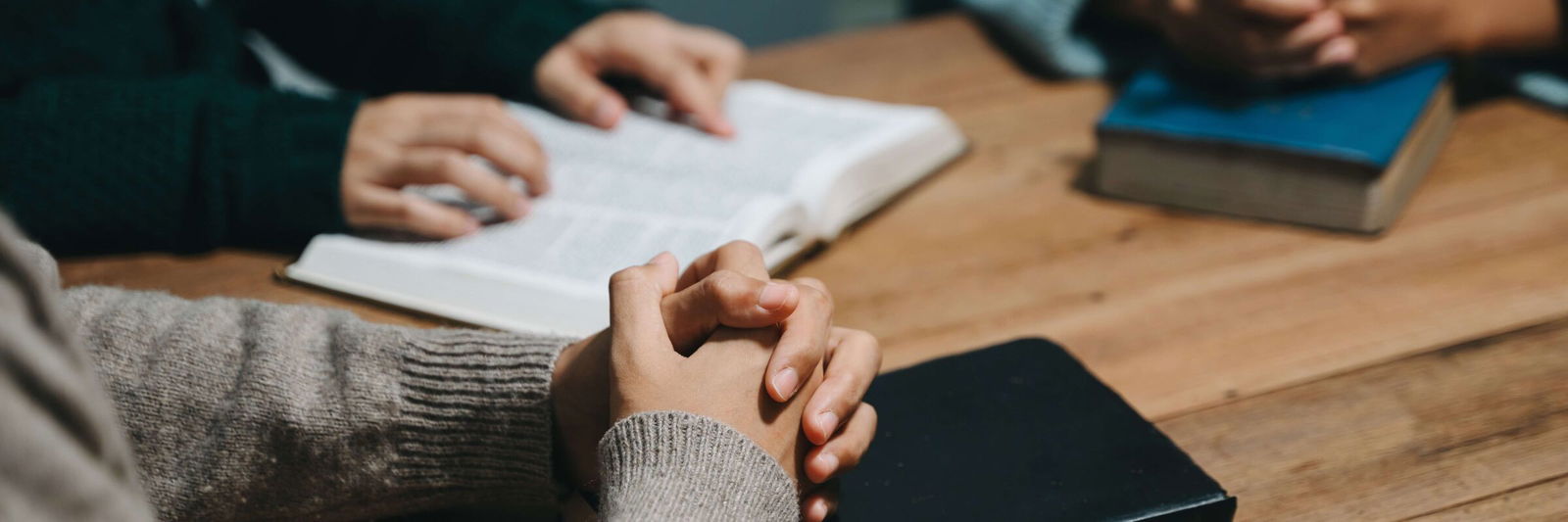 Eine Gruppe von Menschen sitzt an einem Holztisch und spricht über den Glauben, vor ihnen liegen aufgeschlagene Bibeln. 
