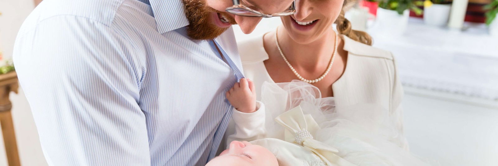 Glückliche Eltern in der Kirche blicken liebevoll auf ihr Baby, das sie zur Taufe in den Armen halten.