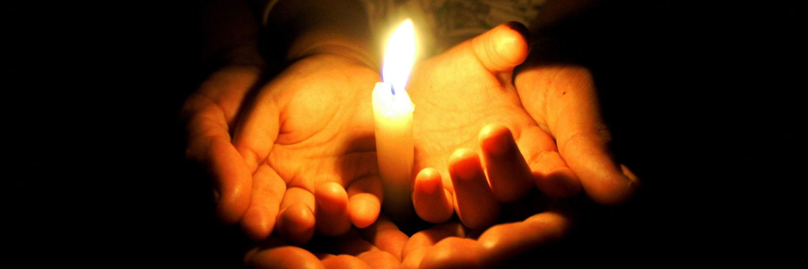 In zwei geöffneten Händen brennt eine Kerze – ein Zeichen von Trost und Hoffnung. 