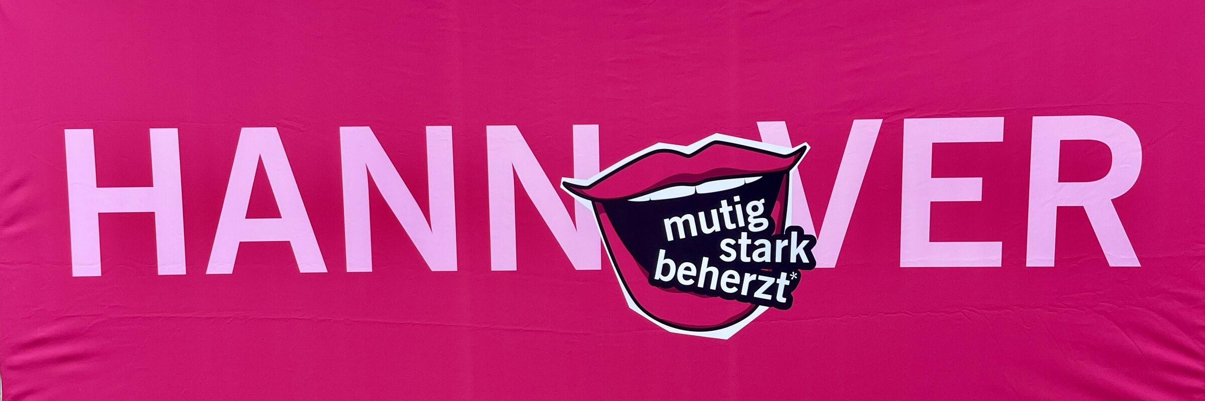 roter Hintergrund, helle Schrift: Hannover, anstelle des O ist ein Kussmund zu sehen, aus dem die Worte kommen "mutig, stark, beherzt".