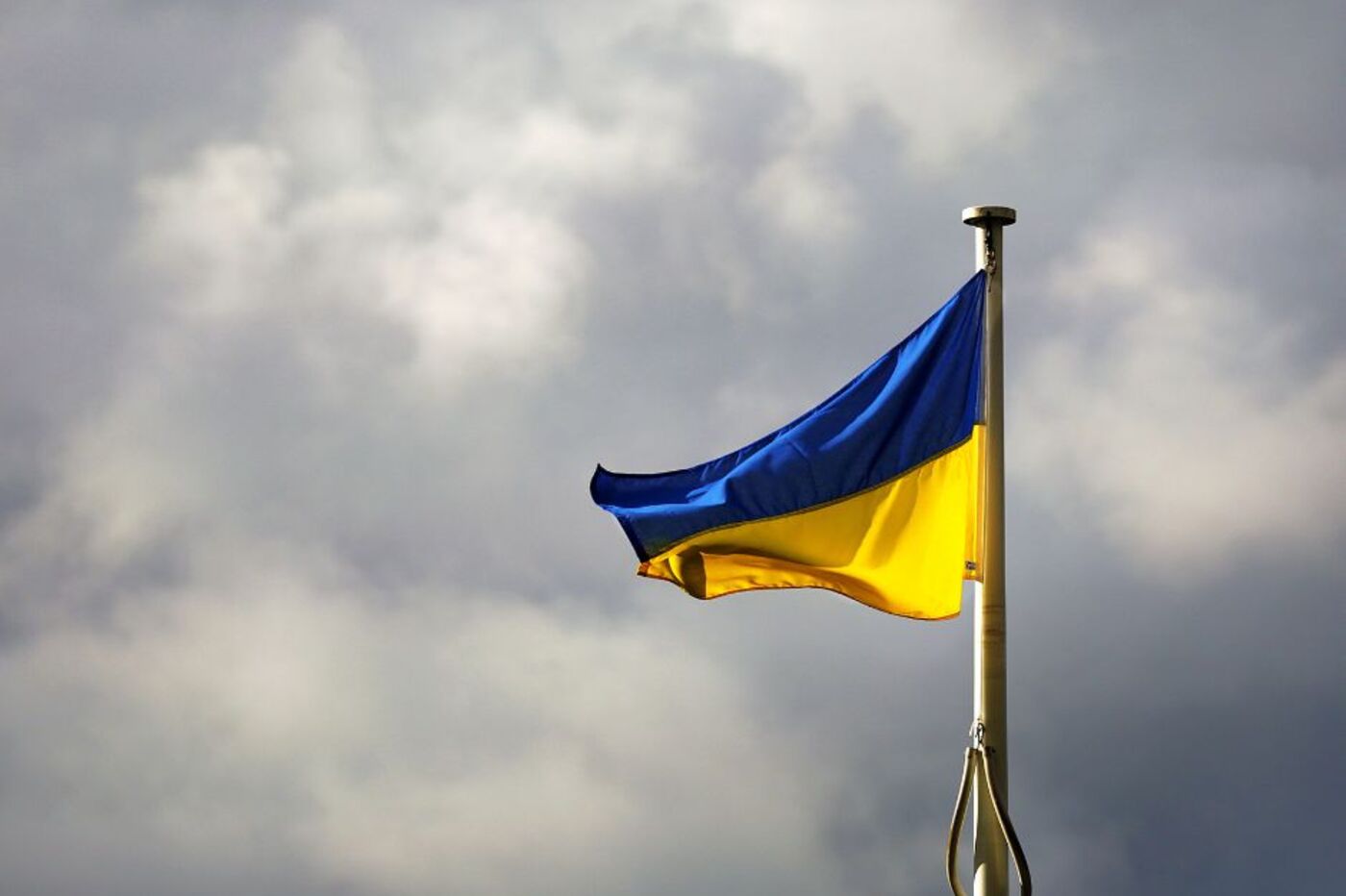 Eine blau-gelbe, ukrainische Flagge weht an einem Mast vor dunklen Wolken.