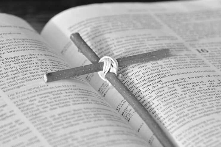 Eine aufgeschlagene Bibel, auf der ein Holzkreuz liegt.