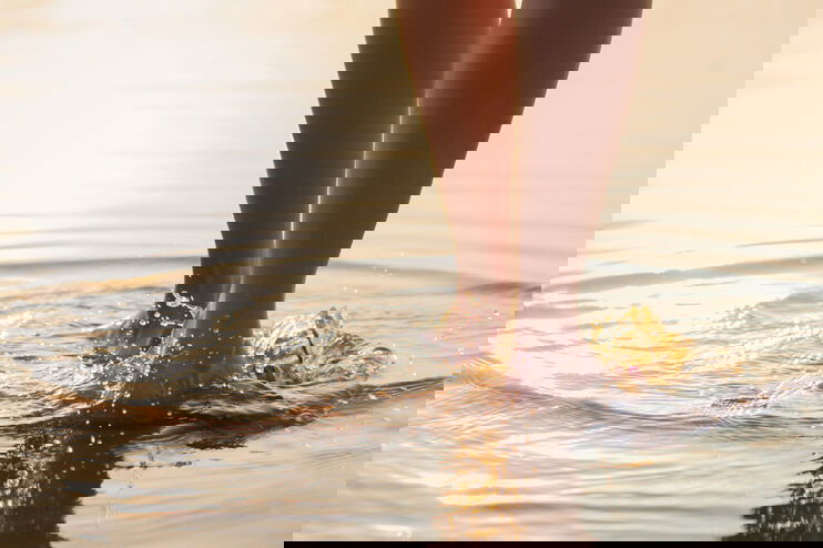 Zwei Füße gehen durchs Wasser.