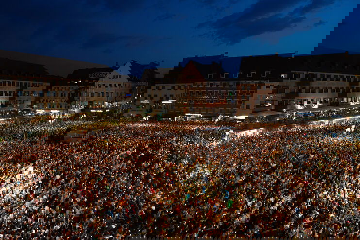 Eine Menschenmenge auf einem großen Marktplatz bei Nacht.