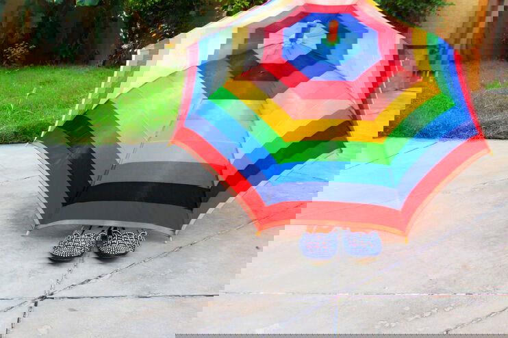 Unter einem bunten Schirm ragt ein Paar Schuhe heraus.