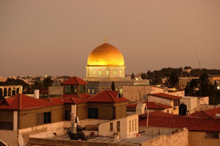 Die goldene Kuppel des Felsendoms ist zu sehen, umgeben von der Stadt Jerusalem. Das Dach des Felsendoms schimmert golden im Sonnenuntergang.