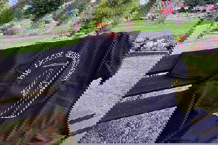 Ein schwarzes T-Shirt mit der Aufschrift „Die letzte Reiseleiterin“ auf einer Friedhofsbank. 