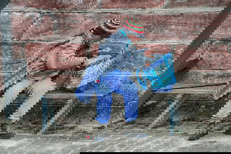 Ein älterer Mann, offenkundig wohnungslos, untersucht den Inhalt seiner Plastiktüte.