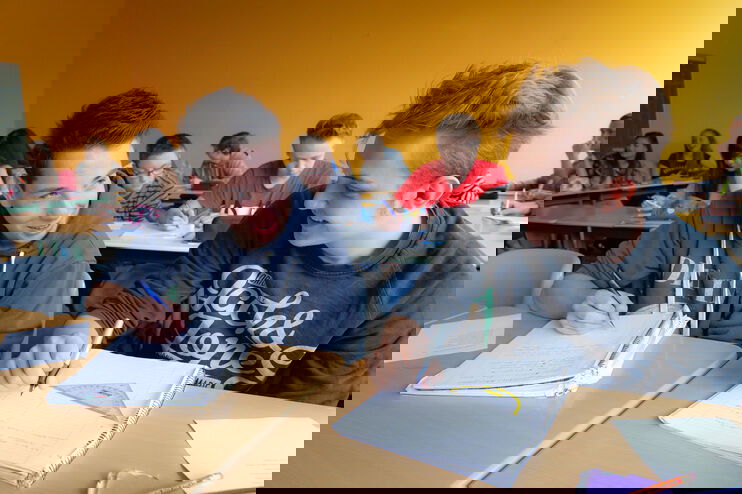 Zwei Schüler sitzen in einem Klassenraum vor ihren Heften und lächeln sich an.