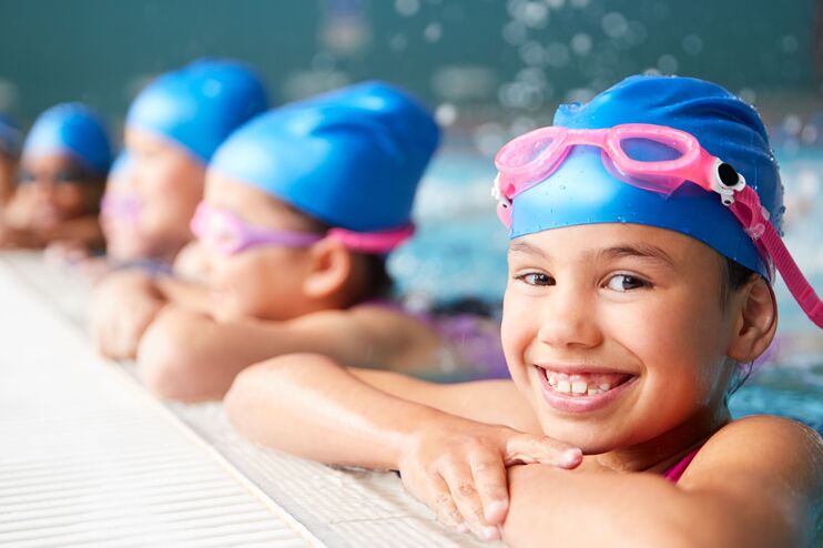eine Gruppe von Kindern im Schwimmbad. Sie lehnen sich am Beckenrand an und lachen.
