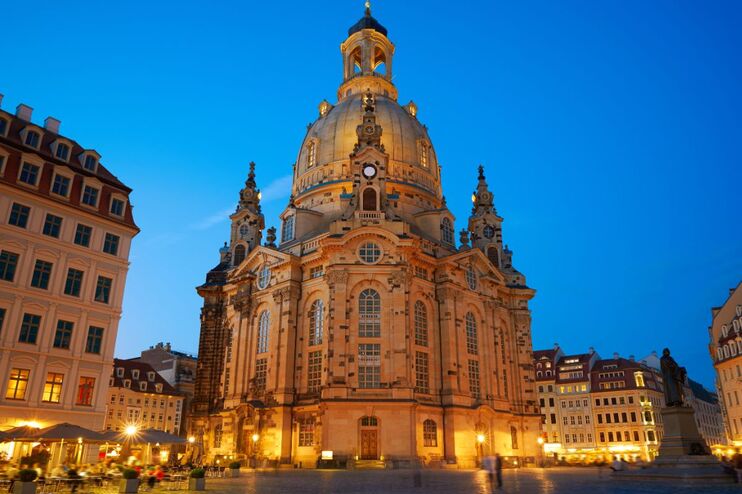Die Frauenkirche Dresden erhebt sich gegen den blau leuchtenden Himmel. Von unten leuchten die Kirche und umliegenden Häuser golden im Licht der Laternen.