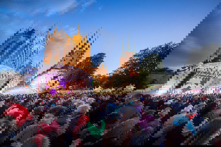 Vor zwei großen Kirchen steht eine Bühne und eine riesige Menschenmenge.