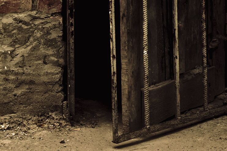 Eine leicht geöffnete Holztür in einer Steinmauer führt in einen dunklen Gang