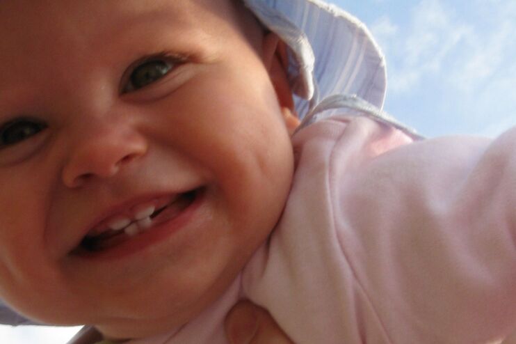 ein Baby wird von jemandem hochgehalten. Es lacht vor Freude