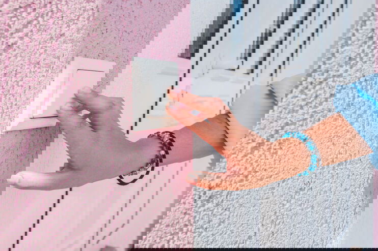 Ein Finger drückt auf einen Klingelknopf an einer rosa Hauswand.