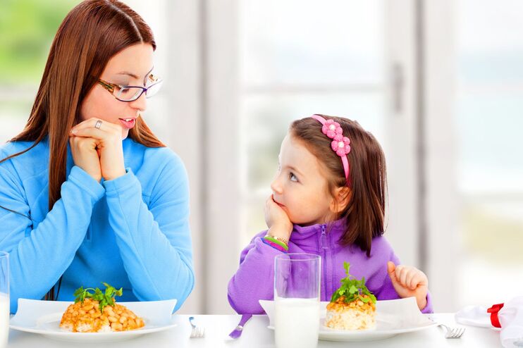 Mutter und Tochter sitzen vor einem gedeckten Tisch.