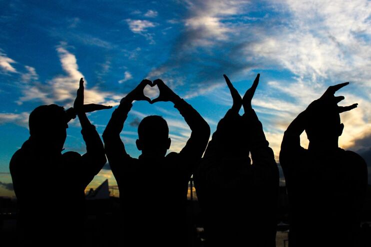 Vier Personen heben sich als Schatten gegen den Himmel ab und formen mit den Händen das Wort "Love"