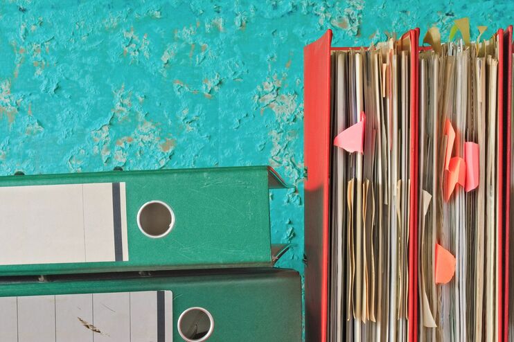 Ein Stapel von Aktenordnern liegt auf einem Regal.