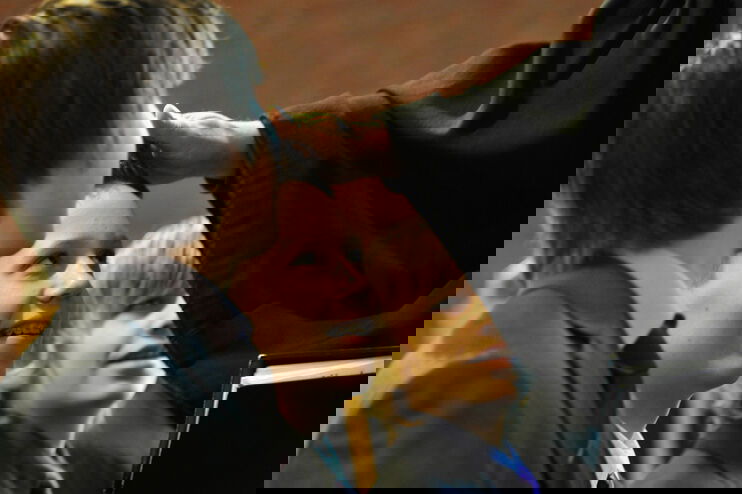 Drei als Jungs lesbare Personen blicken zu einem Pastor auf, der einem von ihnen die Hand auflegt